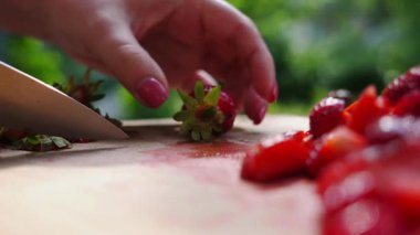 Ahşap bir kesim tahtasında taze çilekleri ustalıkla dilimleyen, açık havada meyvelerin canlı renklerini ve dokularını gösteren yakın çekim dizisi..