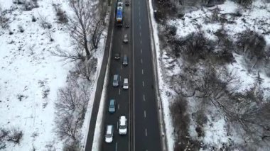 Kış boyunca trafik sıkışıklığı olan yoğun yolun hava görüntüsü, karla kaplı arazide yavaşça hareket eden araçlar, kamera kapları ve dinamik sahne ilerlemesi için yakınlaşmalar