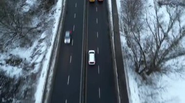 Karla kaplı bir yol boyunca giden arabaların hava görüntüsü, aracın hareketini ve kışın etrafındaki manzarayı gösteriyor, kamera arabaları sorunsuzca takip ediyor. Otomobiller soğuk mevsimde otoyolda gidiyor.