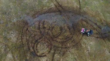 Hava perspektifi, çimenli bir arazide dairesel hareketler yapan bir araç yakalar, geride eşsiz çamur kalıpları bırakır, eylemle doğa arasındaki bağlantıyı gösterir.