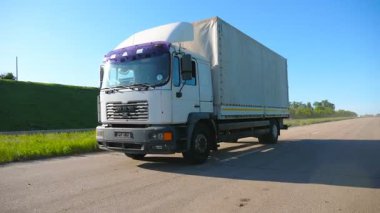 Kamera, kargo karavanıyla otoyolda giden ve malları taşıyan kamyonu takip ediyor. Güneşli bir günde kırsal yoldan geçen bir kamyon. Kargo taşıma konsepti. Yavaş çekim ön görünümü Kapat.