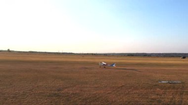 Küçük havaalanındaki çim pistinden küçük bir uçak kalkıyor. Hafif uçak kırsal pistte hareket ediyor ve uçuşa başlıyor. Ultra hafif spor uçak havaalanından ayrıldı. Havacılık konsepti. Hava görünümü.