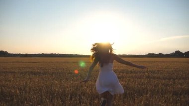 Güzel kız günbatımında buğday alanı çalışıyor. Genç kadın çayır ve enjoing özgürlük koşu. Yaz boş doğa kavramı olarak. Yavaş hareket kapatmak.