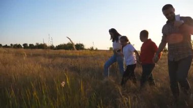 Küçük çocuklu genç ebeveynler gün batımında çim tarlalarında el ele yürürler. İki çocuklu anne ve baba yaz otlaklarında birlikte doğanın tadını çıkarıyorlar. Dolly vurdu..