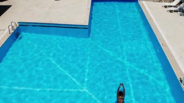 Parlak mavi bir havuzda bireysel yüzme, akışkan hareket ve canlı yansımalar gösterirken, güneş ışığı parlak bir ortam yaratarak yaz tatili ve rahatlığını somutlaştırıyor.