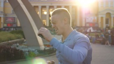 Genç işadamı şehir ortamında başarıyı kutluyor. Başarılı bir adam akıllı telefondan iyi haberler alıyor ve olumlu duygular besliyor. Adam başarıya seviniyor. Yavaş çekim. Yakın çekim..