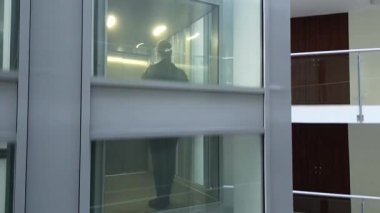 Genç bir kız modern bir asansöre biniyor, kamera düzgün bir şekilde hareket ederken heyecanını sergiliyor, canlı iç mekanı ve asansör boşluğunun parlak tasarımını yakalıyor.