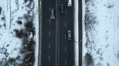 Karla kaplı bir yol boyunca giden arabaların hava görüntüsü, aracın hareketini ve kışın etrafındaki manzarayı gösteriyor, kamera arabaları sorunsuzca takip ediyor. Otomobiller soğuk mevsimde otoyolda gidiyor.