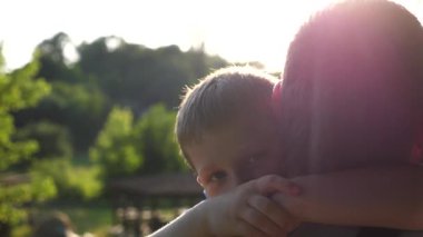 Kırsal kesimde küçük oğlunun elini tutan genç bir baba. Küçük çocuk kameraya bakıyor ve arka planda gün ışığına karşı babasına sarılıyor. Aile mutluluğu kavramı. Yavaşça kapat..