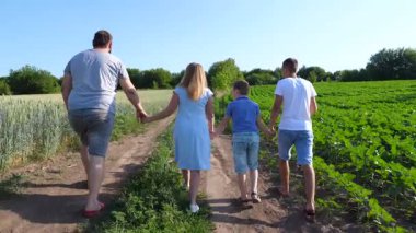 İki oğlu olan genç ebeveynler tarlaların yakınındaki kırsal yolda el ele yürüyorlar. Anne ve baba ve çocuklar yeşil çayırların yakınındaki yolda ilerliyorlar. Aile birlikte vakit geçiriyor..