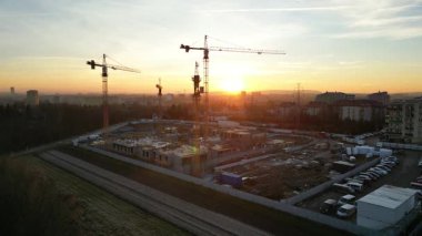 Günbatımında vinçlerle modern yerleşim kompleksinin hava manzarası. İnşaat alanı, turnalarla ve inşaat çalışmalarıyla dolu. Kentsel gelişim kavramı. Gökyüzünün canlı renkleri