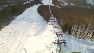 Sandalyeli kar manzaralı kayak pisti, hareket halindeki kayakçıları gösteren hava manzarası, kamera sahneyi sorunsuzca geçiyor, kış manzarasını ve kayak yapmanın heyecanını yakalıyor.