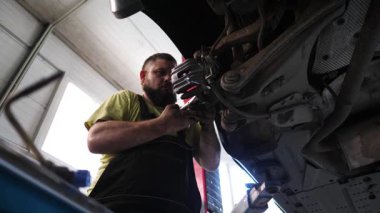 Sakallı yetenekli bir otomotiv teknisyeni, iyi aydınlatılmış garajdaki fren kalibrelerini kaldırmaya odaklanmış, detaylı işçilik ve onarım sürecinde hassasiyet sergiliyor.
