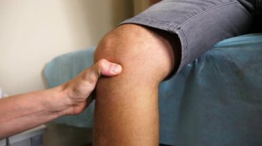 Fizyoterapist diz değerlendirme tekniği uyguluyor, tedavi masasında otururken hastalara baskı uyguluyor, bir klinikte tedavi sürecini ve hasta bakımını gösteriyor..