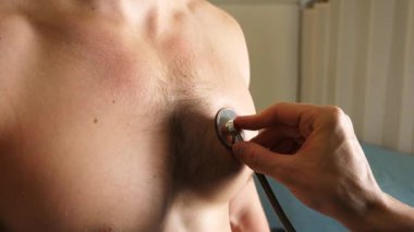 Tıbbi profesyoneller, erkek hasta üzerinde steteskop kullanarak kapsamlı bir muayene yapar, hafif ışıklandırma ve nötr tonlarla klinik bir ortamda özen ve sağlık değerlendirmesi gösterir..
