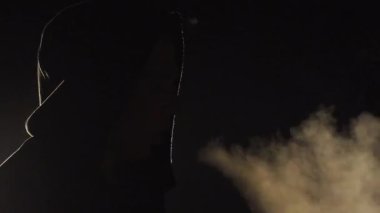 Koyu renk kapüşonlu gizemli figür gecenin karanlığında görünür bir nefes verir. Yumuşak ortam ışığı ve gölgelerle güçlendirilmiş derin bir düşünce ve yalnızlık sahnesi yaratır.