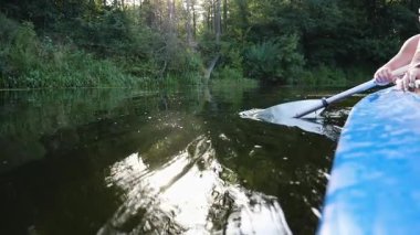 Kano eylemi sahnesinde ritmik raket vuruşları sergiliyor dingin suda sıçramalar yaratıyor, yemyeşil sularla çevrili, açık hava macerasının özünü yakalıyor ve doğayla bağlantı kuruyor..