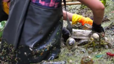 Koruyucu eldivenli kadın çevrecilerin elleri enkaz nehirlerini temizliyor. Kirli gölde plastik şişe toplayan kauçuk elbiseli tanınmayan gönüllüler. Çevre kirliliği koruması.