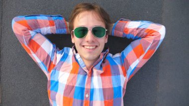 Üstten Görünüm mutlu gencin yalan çatı katında yüksek katlı bina ve gülümseyen güneş gözlüğü. Kameraya bakarak ve zevk gömlekli yakışıklı adam çatıda vakit geçirmek. Yavaş hareket kapatmak.