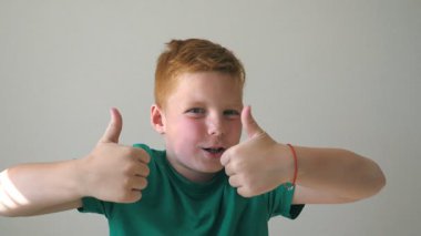 Kapalı alanda çilleri olan mutlu kızıl saçlı çocuğun portresi. Sevimli yakışıklı bebek başarıyı alkışlıyor ve baş parmağını kaldırıyor. Yüzünde neşe ifadesi olan erkek çocuğun duygularını kapat. Yavaş çekim.