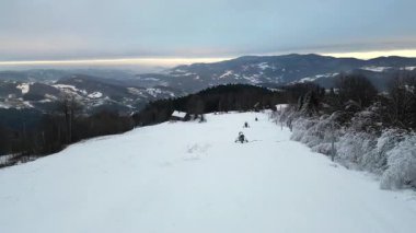 Karla kaplı bir manzaranın havadan görünüşü. Yuvarlanan tepeler ve sakin bir atmosfere sahip uzak dağlar. Kış manzarasının güzelliğini ve doğal elementleri sakin bir ortamda yakalıyor.