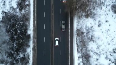 Karla kaplı bir yol boyunca giden arabaların hava görüntüsü, aracın hareketini ve kışın etrafındaki manzarayı gösteriyor, kamera arabaları sorunsuzca takip ediyor. Otomobiller soğuk mevsimde otoyolda gidiyor.