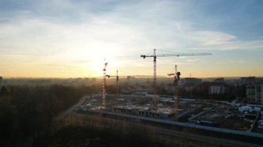 Gün batımından önce aydınlanan inşaat sahasına havadan bakıldığında vinçler ve bina yapıları yer alıyor. Şehrin kenar mahallelerinde modern bir evin inşaatı. Kentsel kalkınma kavramı