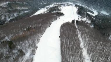 Karlı dağ manzarası, ağaçların arasında dönen kayak izleri, sakin kış atmosferini ve doğanın dokunulmamış karının güzelliğini yansıtıyor.