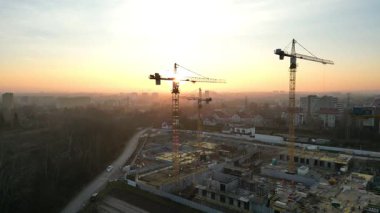 Günbatımında vinçlerle modern yerleşim kompleksinin hava manzarası. İnşaat alanı, turnalarla ve inşaat çalışmalarıyla dolu. Kentsel gelişim kavramı. Gökyüzünün canlı renkleri