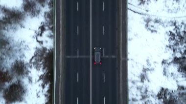 Karla kaplı bir yol boyunca giden arabaların hava görüntüsü, aracın hareketini ve kışın etrafındaki manzarayı gösteriyor, kamera arabaları sorunsuzca takip ediyor. Otomobiller soğuk mevsimde otoyolda gidiyor.