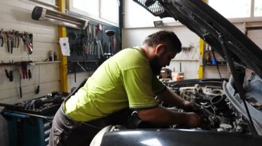 Yetişkin oto tamircisi atölyede arabanın bakımını yapıyor. Garajda kaputun altında çalışan profesyonel bir tamirci. Erkek tamirci iş yerinde otomobil motorunu kontrol ediyor. Aktarım tanısı.