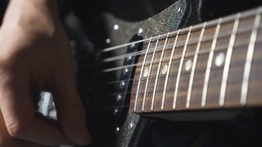 İpleri tıngırdatan gitaristin parmaklarını kapat. Elektro gitarla çalan erkek müzisyenin eli. Yetişkin bir adamın kolu bir müzik aletinde çalar. Yeni bir melodi besteleyen adam. Yavaş çekim.