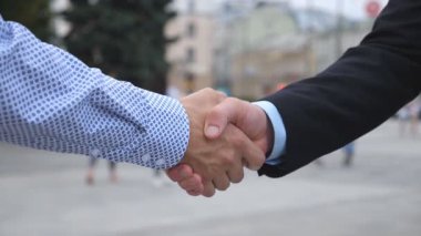 Şehir ortamında birbirini selamlayan iki iş adamı. Bulanık şehir geçmişine sahip genç erkek arkadaşlar el sıkışıyor. İş ortaklarının el sıkışması. Yan Görünüm Yavaşça Kapat.