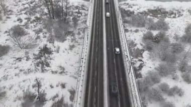 Kar yağışı sırasında karla kaplı bir yolda giden arabaların hava görüntüsü. Kış manzarasını çevreleyen araçlar. Kamera otomobilleri sorunsuz takip ediyor. Otomobiller soğuk mevsimde otoyolda gidiyor.