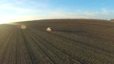 Otlakta giden off-road aracı. Kamyon gün batımında tarladan geçiyor. Arka planda güneş ışığı olan siyah bir araba yolda gidiyor. Tarım çiftçiliği kavramı. Hava görüntüsü.