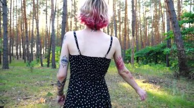 Pembe saçlı kaygısız hippi kadın yaz ormanında eğleniyor. Ormanda gezen dövmeli mutlu, güler yüzlü bir punk kızı. Kulak tünelleri olan genç bayan hippi yaz doğasında dinleniyor..