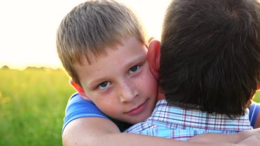 Küçük çocuk kameraya bakıyor ve arka planda parlak güneş ışığına karşı babasına sarılıyor. Kırsalda küçük oğlunun elini tutan genç bir baba. Aile mutluluğu kavramı. Yavaşça kapat..