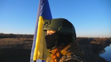Ukraynalı asker kız günbatımının arka planında ulusal bayrağı kaldırdı. Askeri üniformalı genç bayan asker tepenin zirvesinde Ukrayna bayrağı sallıyor. Savaşın zaferi. Dolly vurdu..