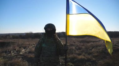 Askeri üniformalı bir kadın güneşli bir günde Ukrayna bayrağını kaldırdı. Kadın Ukraynalı asker ulusal bir bayrak sallıyor. Rus saldırısına karşı zafer. İstila direnişi.