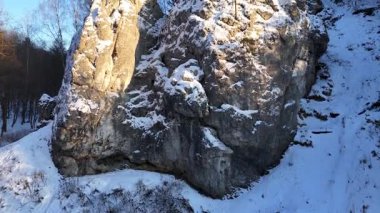 Çam ağaçları ve yüzeyi aydınlatan güneş ışığı ile karla kaplı kayalık uçurum, engebeli arazide yavaş yavaş ışık ve gölgenin geçişini gösteriyor. Hava görünümü