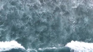 Okyanus dalgalarının kıyıya çarpan hava görüntüsü, denizin yüzeyinde sürekli akan su ve köpüğün dinamik hareketini gösteriyor.