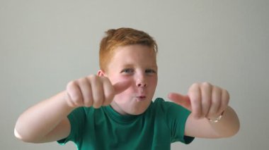 Mutlu kızıl saçlı çilli çocuğun portresi. Sevimli yakışıklı bebek başarıyı alkışlıyor ve baş parmağını kaldırıyor. Yüzünde neşe ifadesi olan erkek çocuğun duygularını kapat. Yavaş çekim.