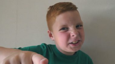 Sevimli yakışıklı bebek seviniyor ve kamerayı işaret ediyor. Kapalı alanda çilleri olan mutlu kızıl saçlı çocuğun portresi. Yüzünde heyecanlı bir ifade olan erkek çocuğun duygularını kapat. Yavaş çekim.