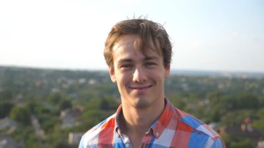 Şehrin arka planında çatıda oturan mutlu genç adamın portresi. Yüzünde neşe ifadesi olan kameraya bakan yakışıklı adam. Mutlu insanın samimi duyguları. Dolly çekim ağır çekim.