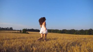 Genç kız mavi gökyüzünün altında buğday tarlası boyunca koşuyor. Kadın çayırda koşuyor. Yan görünüm Yavaş çekim.