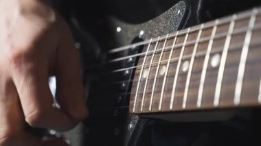 İpleri tıngırdatan gitaristin parmaklarını kapat. Elektro gitarla çalan erkek müzisyenin eli. Yetişkin bir adamın kolu bir müzik aletinde çalar. Yeni bir melodi besteleyen adam. Yavaş çekim.