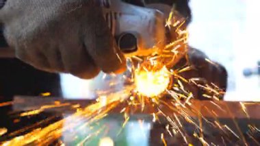 Metal işlemede dairesel testere ile detaylı görüş. Makinistin elleri enstrüman tutuyor ve metali öğütüyor. Garajda ya da atölyede demir kesen bir işçi. Parlak kıvılcımlar uçuşuyor. Kapat..