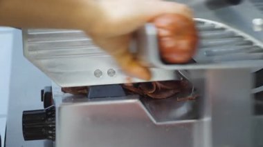 Aşçı kolu mutfak restoranında salam için kesme makinesi kullanıyor. Mutfakta elektrikli yemek dilimleyicisi üzerinde sosis doğrayan şefin erkek eli. Pizza pişirmek için gerekli malzemeleri hazırlama süreci. Kapat..