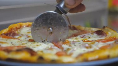 Şefin erkek elini kapayın. Lezzetli pizzayı tabaktaki yuvarlak bıçakla dilimleyin. Aşçının kolu, mutfak restoranında lezzetli pepperonili pizzayı parçalara ayırır. Yavaş çekim.