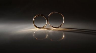 Zarif alyanslar yansıtıcı bir yüzeyde sergileniyor. Karmaşık tasarımlarını ve yumuşak aydınlatmalarını vurguluyor. Romantik bir ortamda aşkı ve bağlılığı simgeliyor.